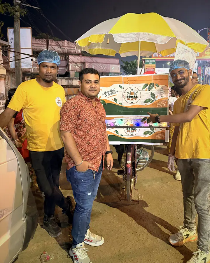 A visitor posing with two crew members in front of the branded cart